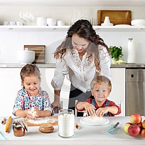 Studio shot of a family in the kitchen at home. Small children, a girl and a boy, learn to make dough rolls with their mother or