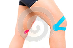 Studio shot of a female patient with kinesio tape on her knee, isolated over white. Kinesiology, physical therapy.