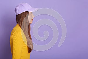 Studio shot of female wearing baseball cap and yellow shirt, side view of attractive female looking straight ahead. Copy space of