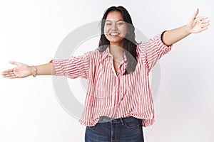 Studio shot of friendly outgoing and sincere young asian girl likes cuddles and hugs extending hands sideways wide and photo