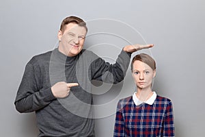 Tall man is showing height of short woman and pointing at her photo