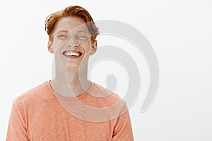 Studio shot of handsome confident adult redhead guy with freckles and bright smile, grinning joyfully and gazing