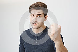 Studio shot of handsome european male model showing fist to camera and lifting eyebrows, demanding something over gray