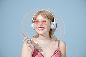 Studio shot of happy Asian millennial girl smiles gladfully looks away uses smartphone and headphone