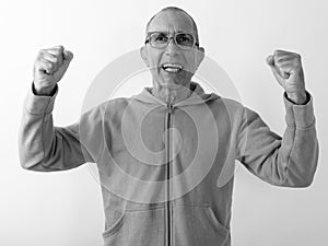 Studio shot of happy bald senior man smiling and looking excited while wearing eyeglasses against white background