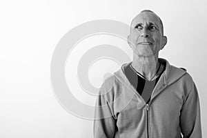 Studio shot of happy bald senior man smiling and thinking against white background