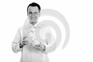 Studio shot of happy crazy man doctor smiling while holding two piggy banks on top of each other