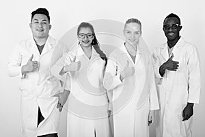 Studio shot of happy diverse group of multi ethnic doctors smiling while giving thumb up together