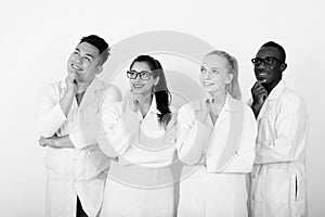 Studio shot of happy diverse group of multi ethnic doctors smiling and thinking while looking up together