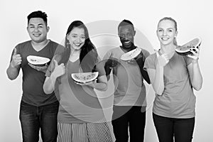 Studio shot of happy diverse group of multi ethnic friends smiling while holding slice of watermelon and giving thumb up