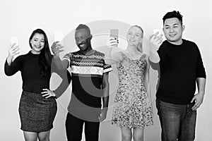 Studio shot of happy diverse group of multi ethnic friends smiling while taking selfie pictures with mobile phones