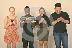 Studio shot of happy diverse group of multi ethnic friends smiling while using mobile phones together
