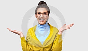 Studio shot of happy excited young beautiful woman in blue, yellow outfit and round transparent glasses, smiling broadly