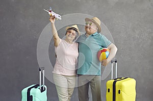 Studio shot of happy senior couple in sunglasses and hats holding a paper airplane