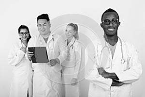 Studio shot of happy young African man doctor with arms crossed and diverse group of multi ethnic doctors smiling while