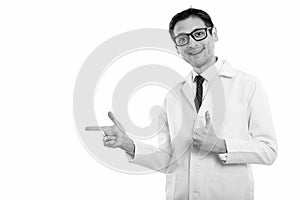 Studio shot of happy young man doctor smiling while pointing to the side and giving thumb up