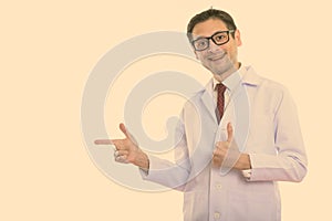 Studio shot of happy young man doctor smiling while pointing to the side and giving thumb up
