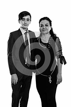 Studio shot of happy young Persian teenage businessman and mature Persian woman smiling while standing together