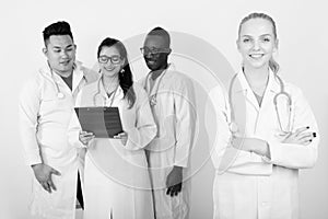 Studio shot of happy young woman doctor with arms crossed and diverse group of multi ethnic doctors smiling while