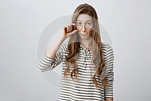 Studio shot of impressed young girl with blond hair, taking off glasses and looking from under forehead, pouting, being