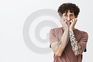 Studio shot of intense scared and timid good-looking funny european guy with moustache curly hair and tattoos biting