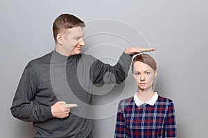 Tall man is showing height of short woman and pointing at her