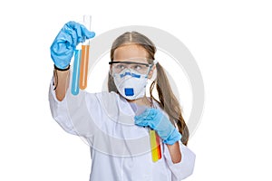 Studio shot of little cute girl, kid in white big gown as chemist, scientist doing experiment with colored chemical