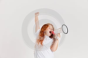Studio shot of little girl, kid in casual style clothes shouting at megaphone isolated over white background. News