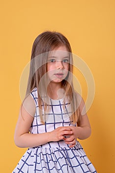 Studio shot of a  little serious girl with long blonde hair  against yellow background