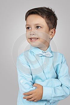 Studio shot of little smiling boy wearing blue shirt and a tie - bow on a white background