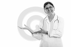 Studio shot of mature happy woman doctor smiling and showing something