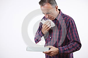 Studio Shot Of Mature Man With Cold Or Flu Virus Sneezing Into Paper Tissue Against White Background