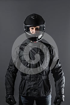 Studio shot of Motorcyclist biker in black equipment looking at camera.