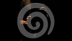 Studio shot of old retro hardcover book on dark background in warm light. Man holding closed old vintage book in hands