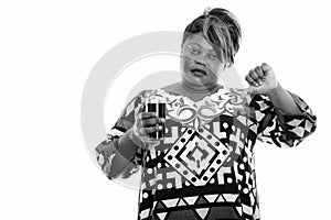 Studio shot of overweight African woman holding glass of soda drink and giving thumb down