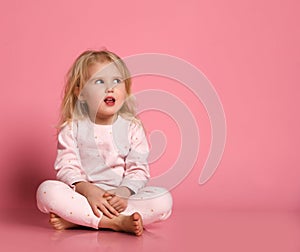 Studio shot of pleased beautiful young woman posing in eyemask. Cheerful Little cute girl in pajamas sits on the floor on pink photo
