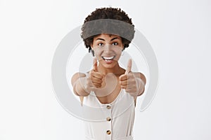 Studio shot of pleased and satisfied supportive woman with afro hairstyle pulling hands towards camera and showing