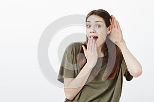 Studio shot of positive good-looking woman with brown hair, tilting right while overhearing interesting conversation