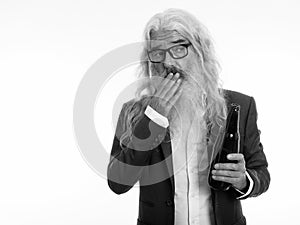 Studio shot of senior bearded businessman holding bottle of beer and looking shocked