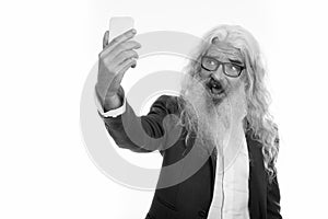 Studio shot of senior bearded businessman taking selfie picture with mobile phone