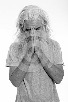 Studio shot of senior bearded man crying while looking down and covering face