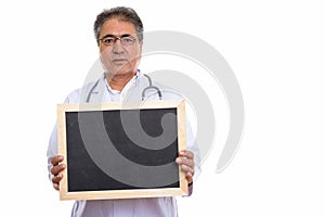 Studio shot of senior Persian man doctor holding blank blackboar