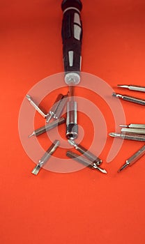 A set of a screwdriver with replaceable bits and bits for her for working with small parts on a red background