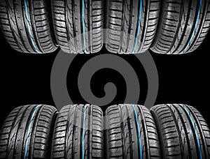 Studio shot of a set of summer car tires on black background. Tire stack background. Car tyre protector close up. Black rubber tir