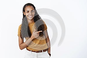Studio shot of shy and cute pretty young african american woman with long curly hair bending as pointing right with