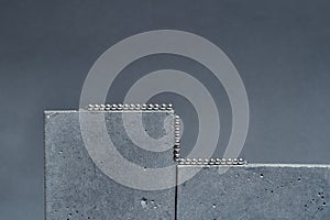 Studio shot of silver metal ball necklace on concrete elements isolated over gray background