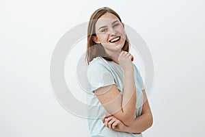 Studio shot of skillful creative and ambitious european woman in trendy t-shirt standing in profile over white wall