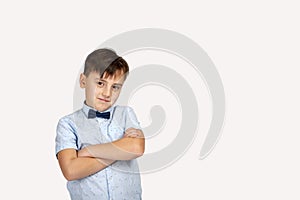 Studio shot of a smiling boy wearing a blue shirt and bow tie with arms crossed on grey background