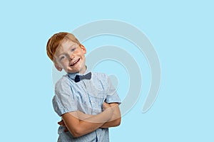 Studio shot of a smiling redhead  boy wearing   blue  shirt with bow against   blue background with copy space