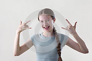 Studio Shot Of Smiling Teenage Girl Making Rebellious Rock And Roll Hand Gesture Looking Into Camera